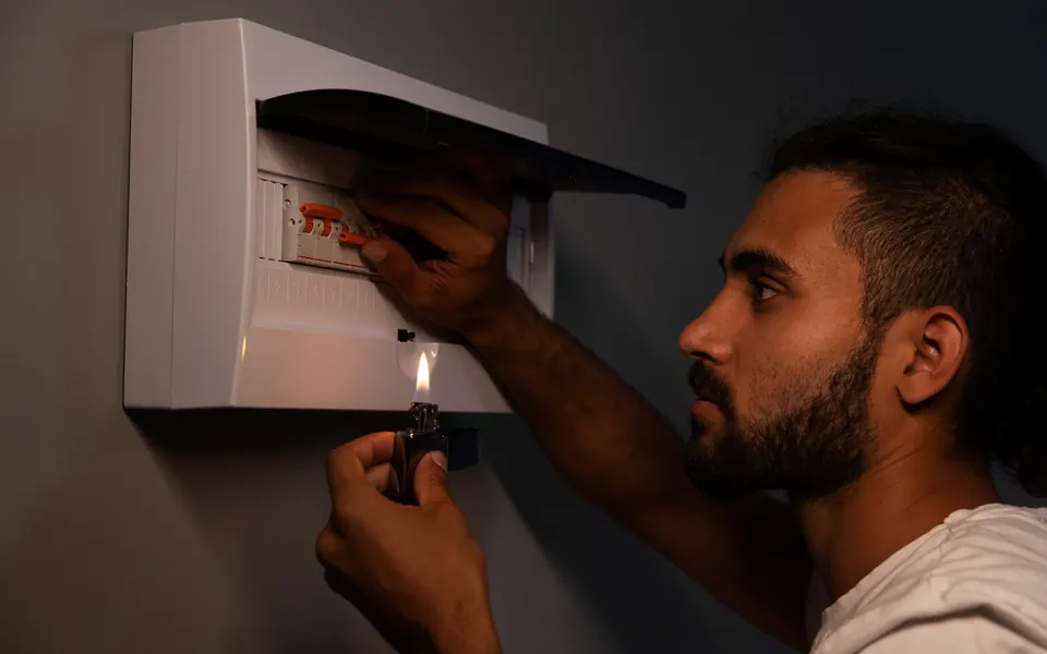 Al buio, un uomo fa luce sul quadro elettrico con un accendino
