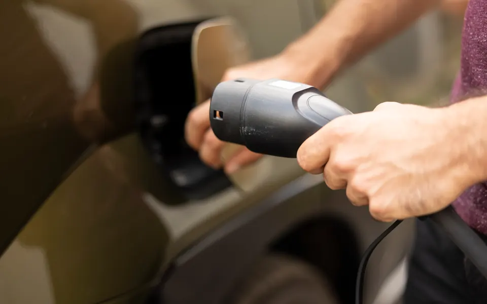 Una mano infila il connettore di ricarica nella presa di un'auto elettrica